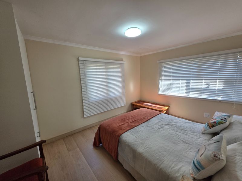 A well-maintained bedroom featuring light laminate flooring, built-in cupboards, and dual windows fitted with venetian blinds.