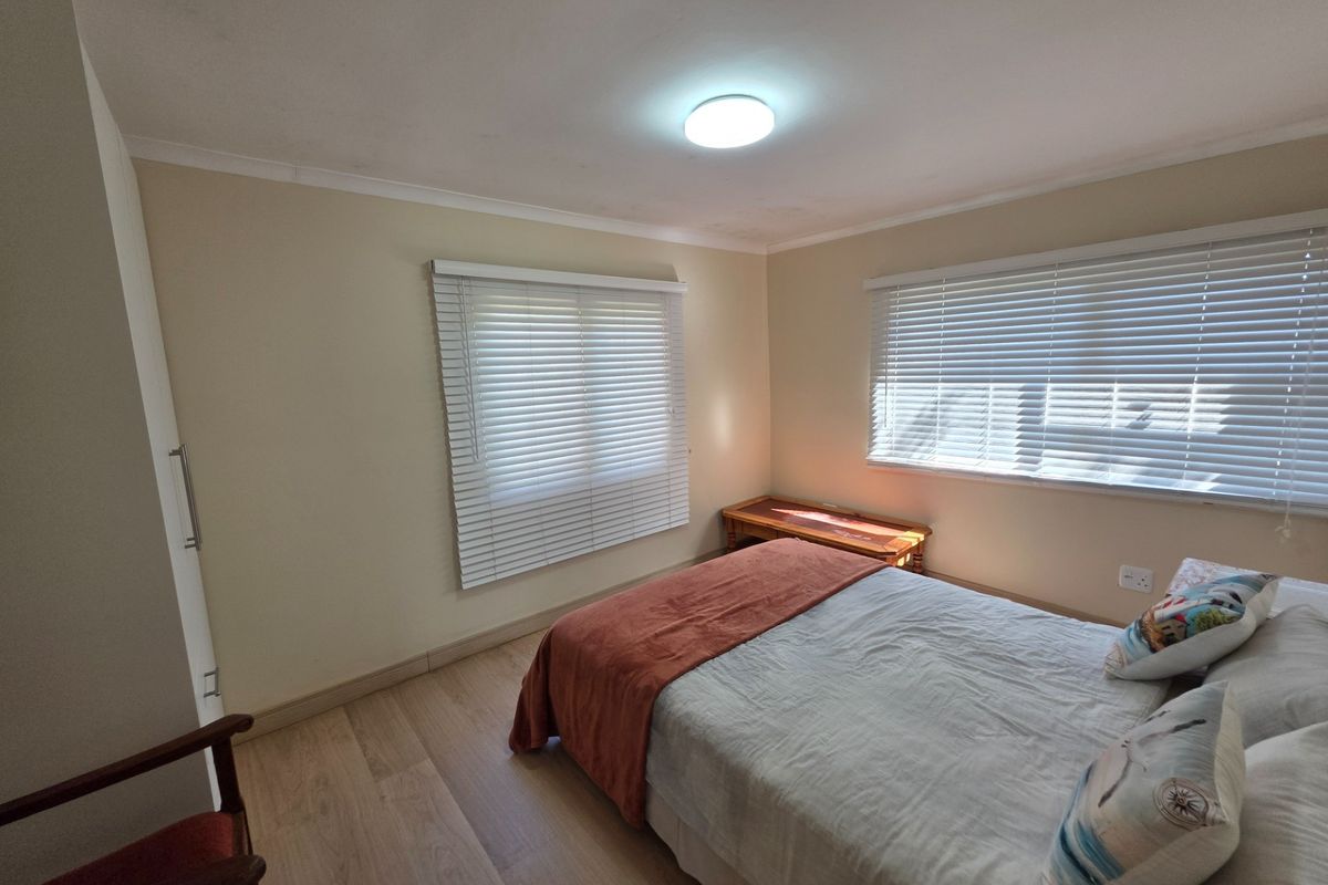 A well-maintained bedroom featuring light laminate flooring, built-in cupboards, and dual windows fitted with venetian blinds.