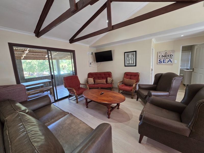 Spacious living room featuring vaulted ceilings with exposed timber beams, light laminate flooring, and large sliding glass doors leading to an outdoor patio area.