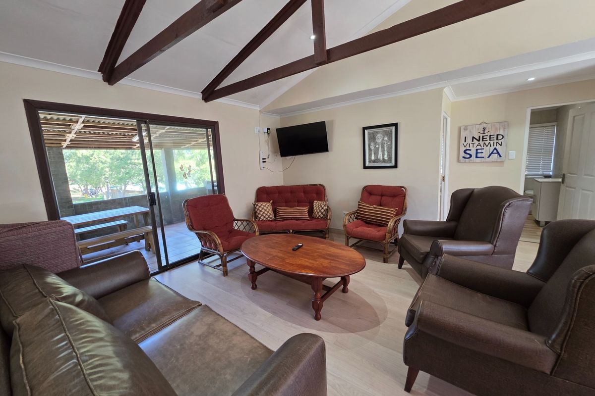 Spacious living room featuring vaulted ceilings with exposed timber beams, light laminate flooring, and large sliding glass doors leading to an outdoor patio area.