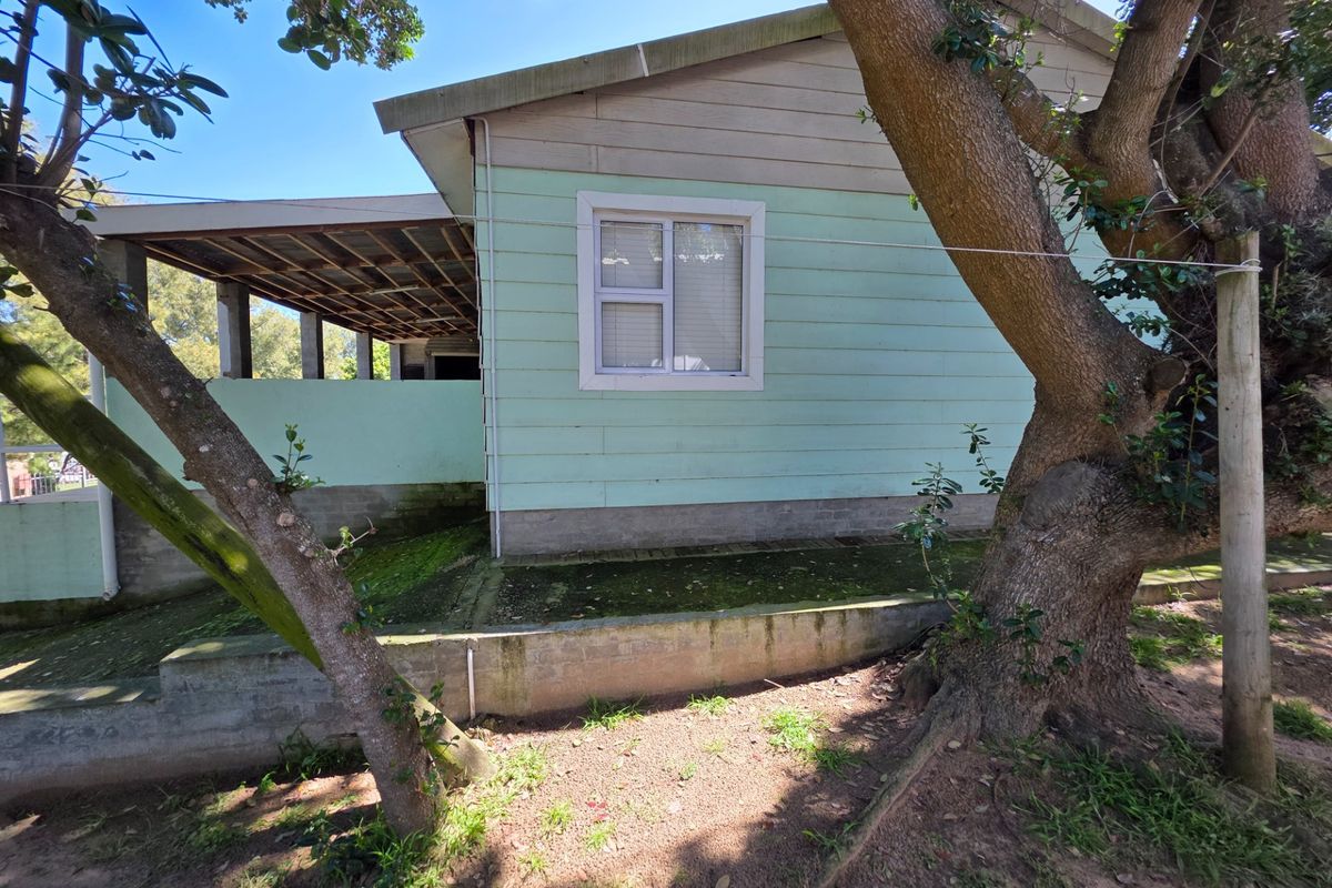 Rear view of the property featuring timber cladding, a concrete retaining wall, and a covered patio area with visible signs of weathering.