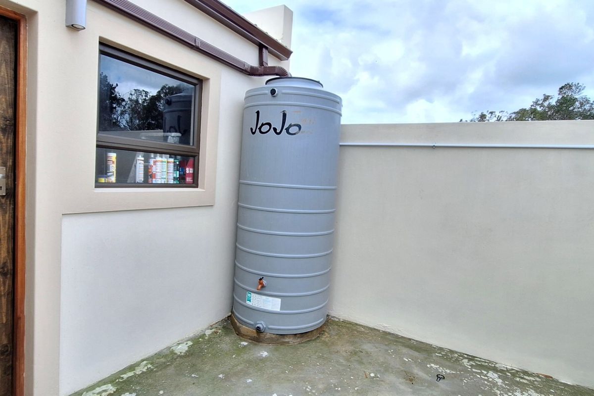 Rear exterior area featuring a water storage tank, guttering system, and concrete flooring adjacent to the building wall.