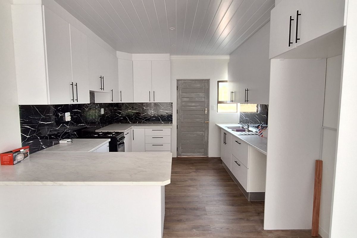 Modern kitchen featuring white cabinetry, black marble-look splashbacks, stone-look countertops, a breakfast bar, and timber-look flooring in a clean, open layout.
