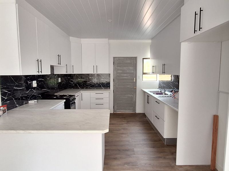 Modern kitchen featuring white cabinetry, black marble-look splashbacks, stone-look countertops, a breakfast bar, and timber-look flooring in a clean, open layout.