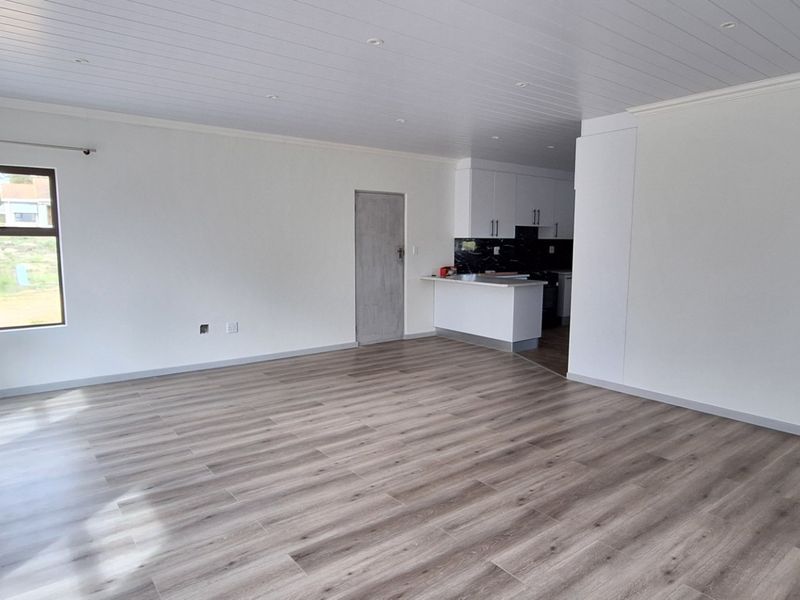 Spacious open-plan living area featuring modern laminate flooring, a tongue and groove ceiling with recessed lighting, and an adjoining kitchen space.