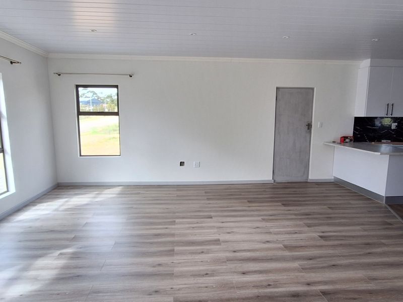 A bright and spacious open-plan living area featuring modern laminate flooring, a clean white ceiling, and a sleek kitchen with a breakfast bar.