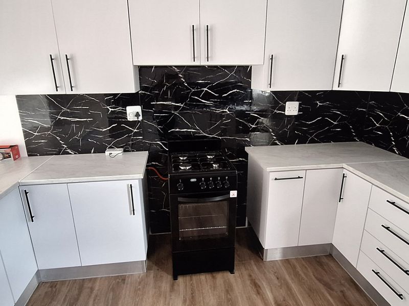 Modern kitchen featuring white cabinetry, marble-effect splashback, laminate countertops, and a freestanding stove.