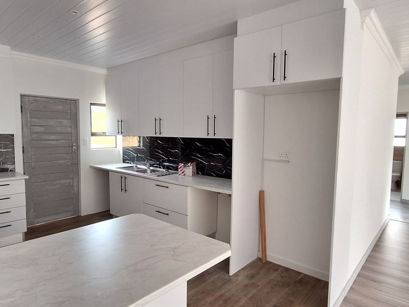 A modern, bright kitchen featuring white cabinetry, marble-look splashbacks, laminate countertops, and a clean, minimalist aesthetic with wood-look flooring.
