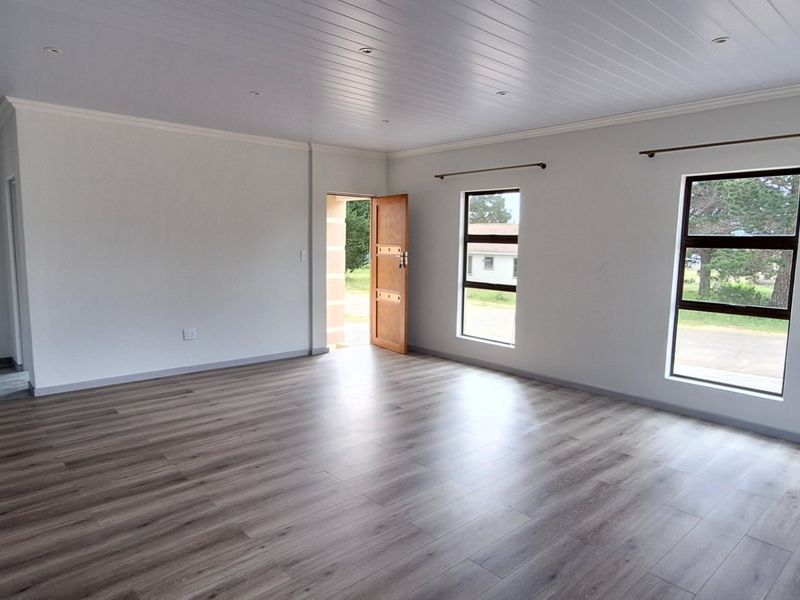 A bright, spacious, and empty living area featuring modern laminate flooring, a clean tongue and groove ceiling, and large windows providing natural light.
