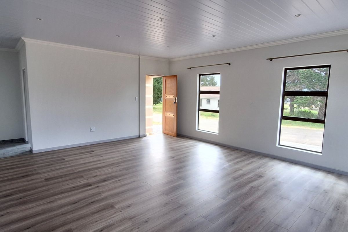 A bright, spacious, and empty living area featuring modern laminate flooring, a clean tongue and groove ceiling, and large windows providing natural light.