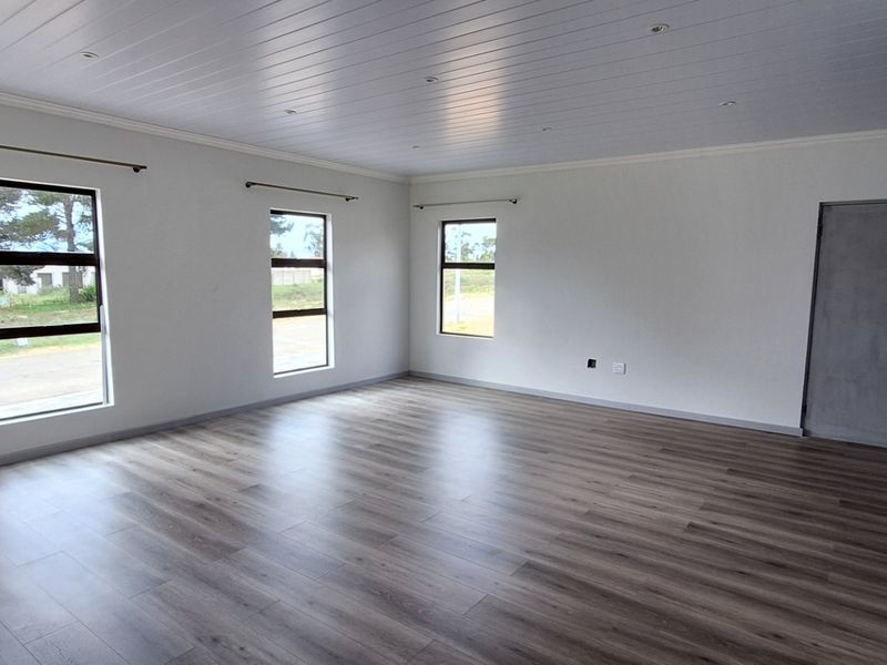 A spacious, empty living area featuring modern laminate flooring, a white tongue and groove ceiling with recessed lighting, and large aluminium-framed windows.
