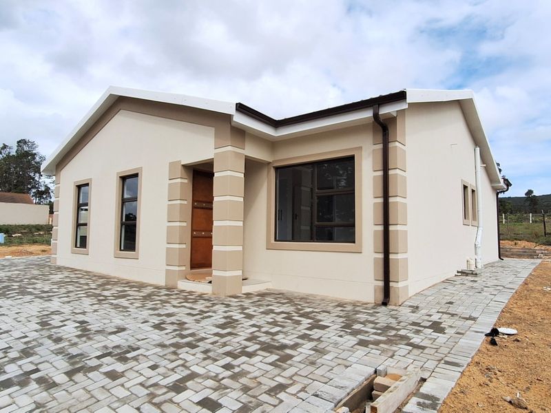 A modern, newly constructed single-story house featuring a paved driveway, clean plastered exterior, and contemporary aluminium window frames in a quiet residential setting.