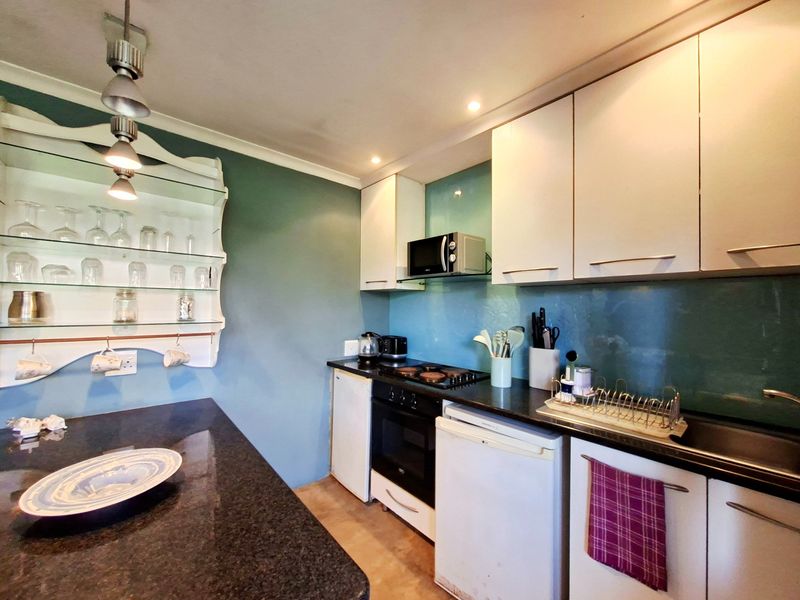Compact kitchen featuring white cabinetry, dark granite countertops, glass splashbacks, and integrated appliances, offering a functional and efficient workspace.
