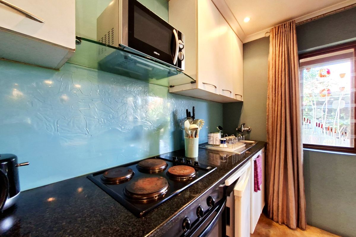 Compact kitchen featuring granite countertops, a glass splashback, built-in oven, electric hob, and integrated microwave with ample upper and lower cabinetry.