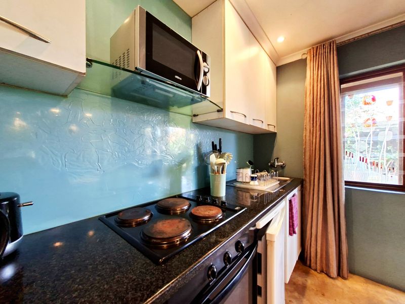 Compact kitchen featuring granite countertops, a glass splashback, built-in oven, electric hob, and integrated microwave with ample upper and lower cabinetry.