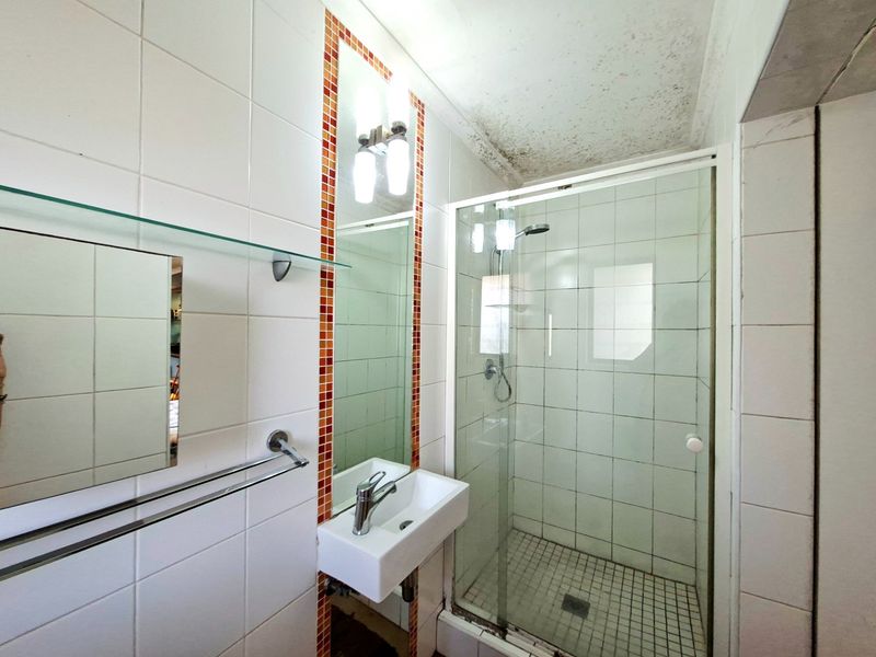 Compact bathroom featuring a glass-enclosed shower, wall-mounted basin, and tiled finishes. The space requires maintenance to address ceiling staining and grout wear.