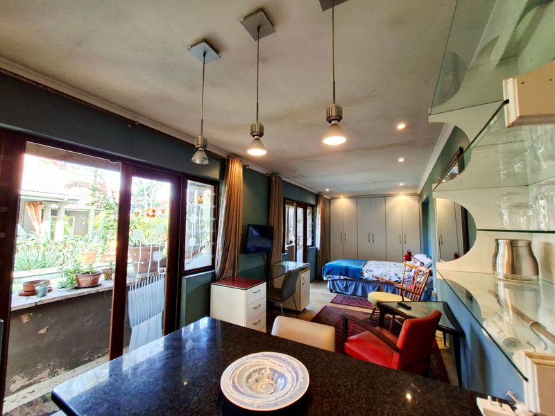 A multi-functional bedroom space featuring built-in cupboards, pendant lighting, and sliding glass doors leading to an outdoor area with a granite-topped counter.