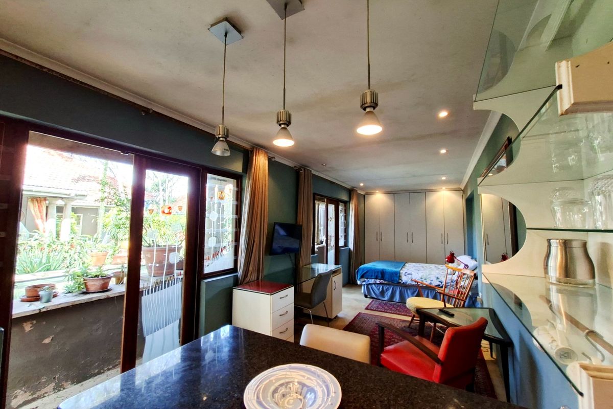 A multi-functional bedroom space featuring built-in cupboards, pendant lighting, and sliding glass doors leading to an outdoor area with a granite-topped counter.