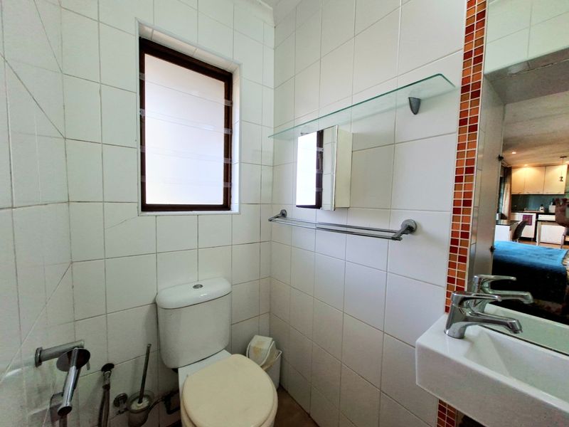 Compact bathroom featuring white wall tiles with decorative mosaic accents, a wall-mounted basin, and a toilet.