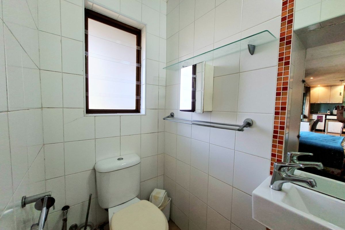 Compact bathroom featuring white wall tiles with decorative mosaic accents, a wall-mounted basin, and a toilet.