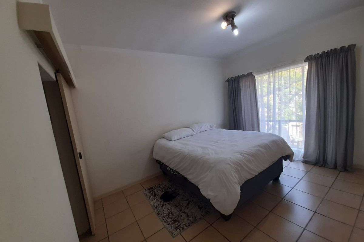A functional bedroom featuring tiled flooring, a built-in cupboard, and a sliding door providing access to natural light.