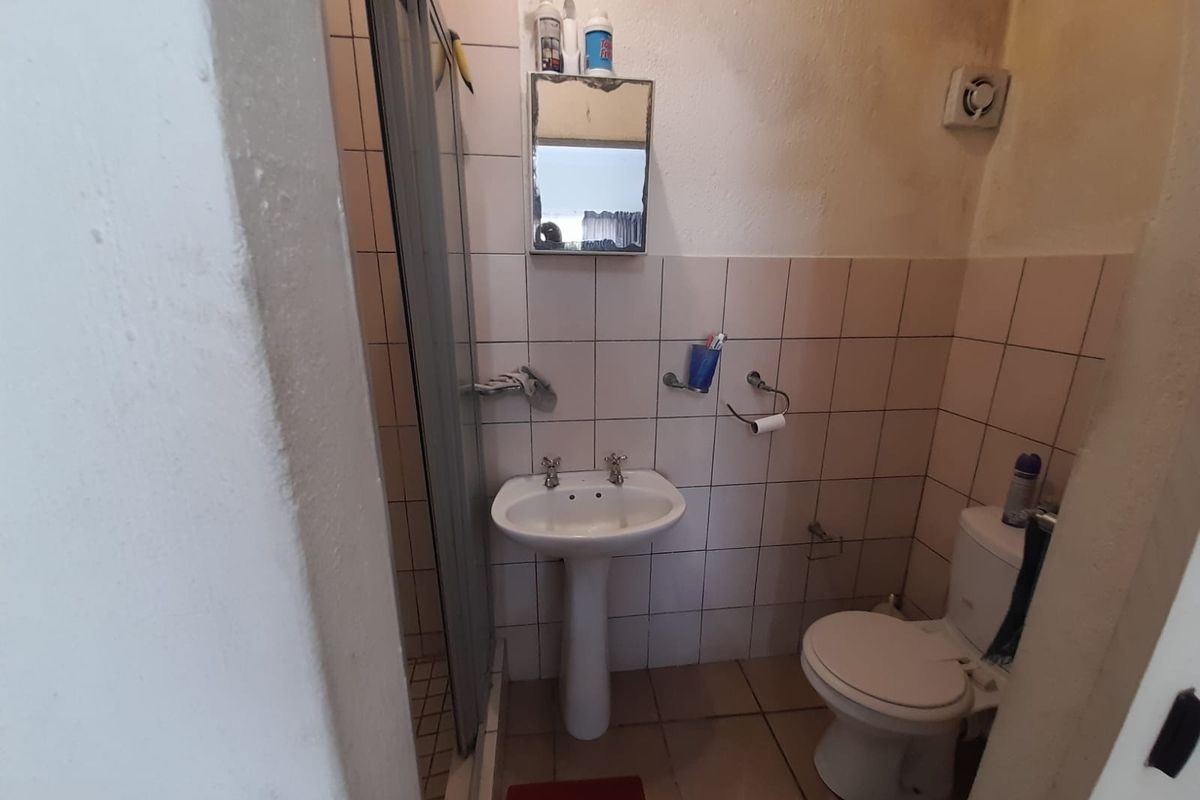 A compact bathroom featuring a pedestal basin, toilet, and shower enclosure with tiled finishes, requiring cosmetic updates to improve its overall condition.