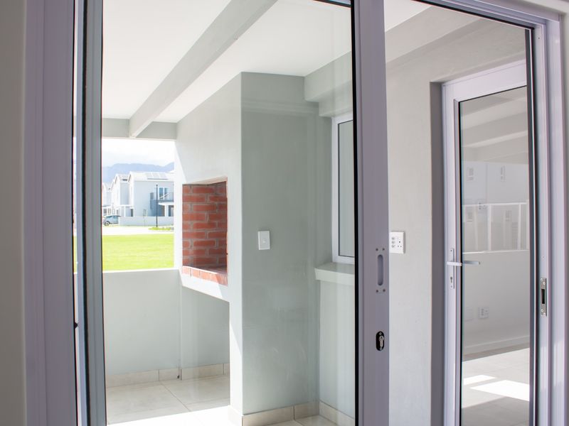 Covered patio featuring a built-in brick braai, tiled flooring, and sliding glass doors providing access to the outdoor area.