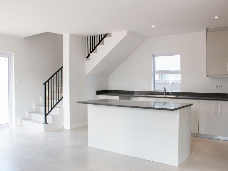Modern open-plan kitchen featuring a central island, stone countertops, sleek cabinetry, and a staircase with a contemporary metal balustrade.