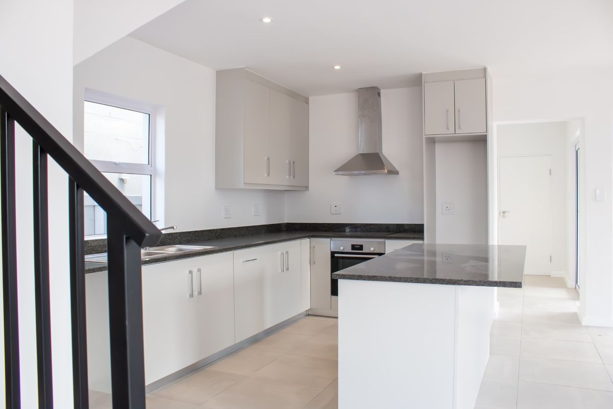 Modern kitchen featuring white cabinetry, granite countertops, stainless steel appliances, and tiled flooring in an open-plan layout.