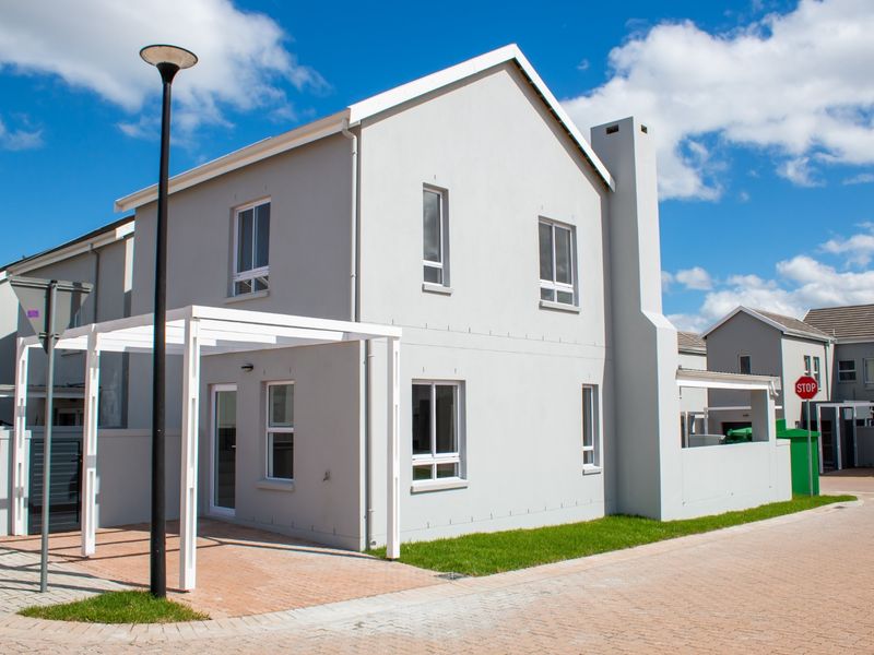 A modern two-story residential house featuring a light grey facade, a white pergola, and a paved driveway in a well-maintained estate setting.
