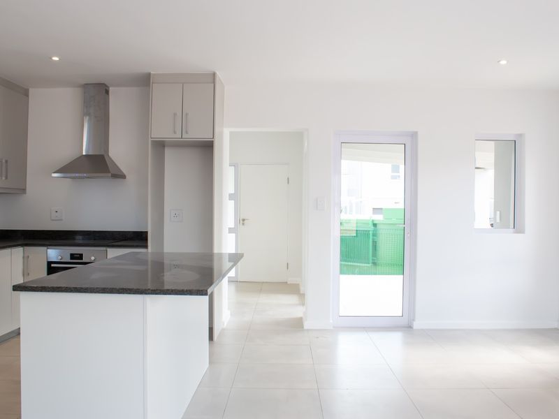 Modern open-plan kitchen featuring sleek cabinetry, granite countertops, stainless steel appliances, and tiled flooring with direct access to an outdoor area.