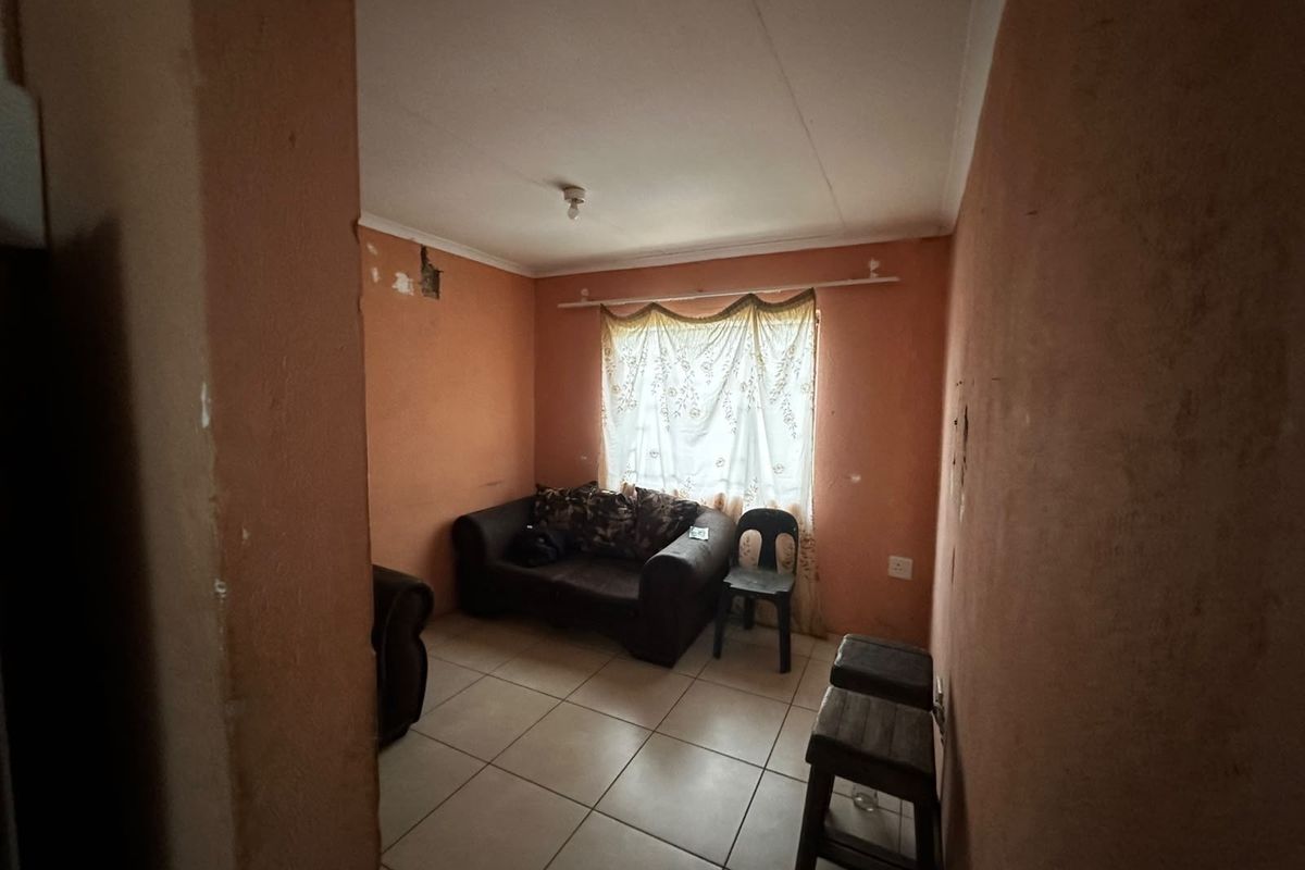 A small living area featuring tiled flooring and plain walls, currently requiring cosmetic updates and plaster repairs to improve the overall finish.
