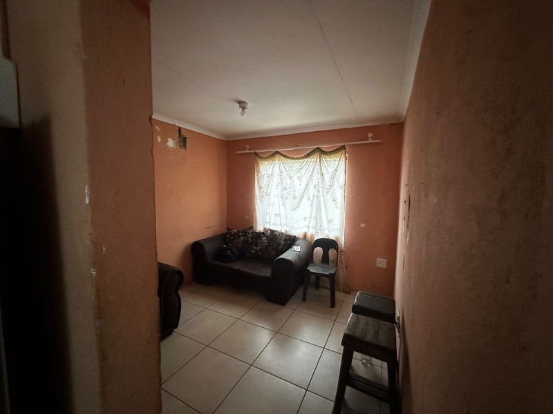 A small living area featuring tiled flooring and plain walls, currently requiring cosmetic updates and plaster repairs to improve the overall finish.