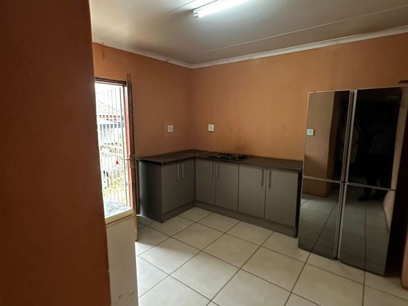 A functional kitchen featuring grey built-in cabinetry, laminate countertops, a built-in hob, and ceramic floor tiles with direct access to the exterior.