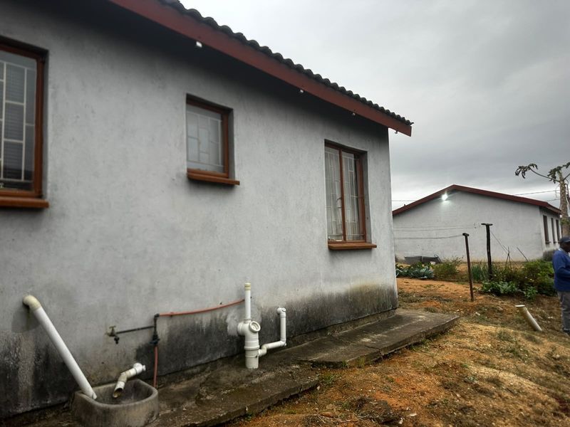 Rear exterior view of the property showing concrete apron, external plumbing fixtures, and visible signs of rising damp on the lower wall sections.