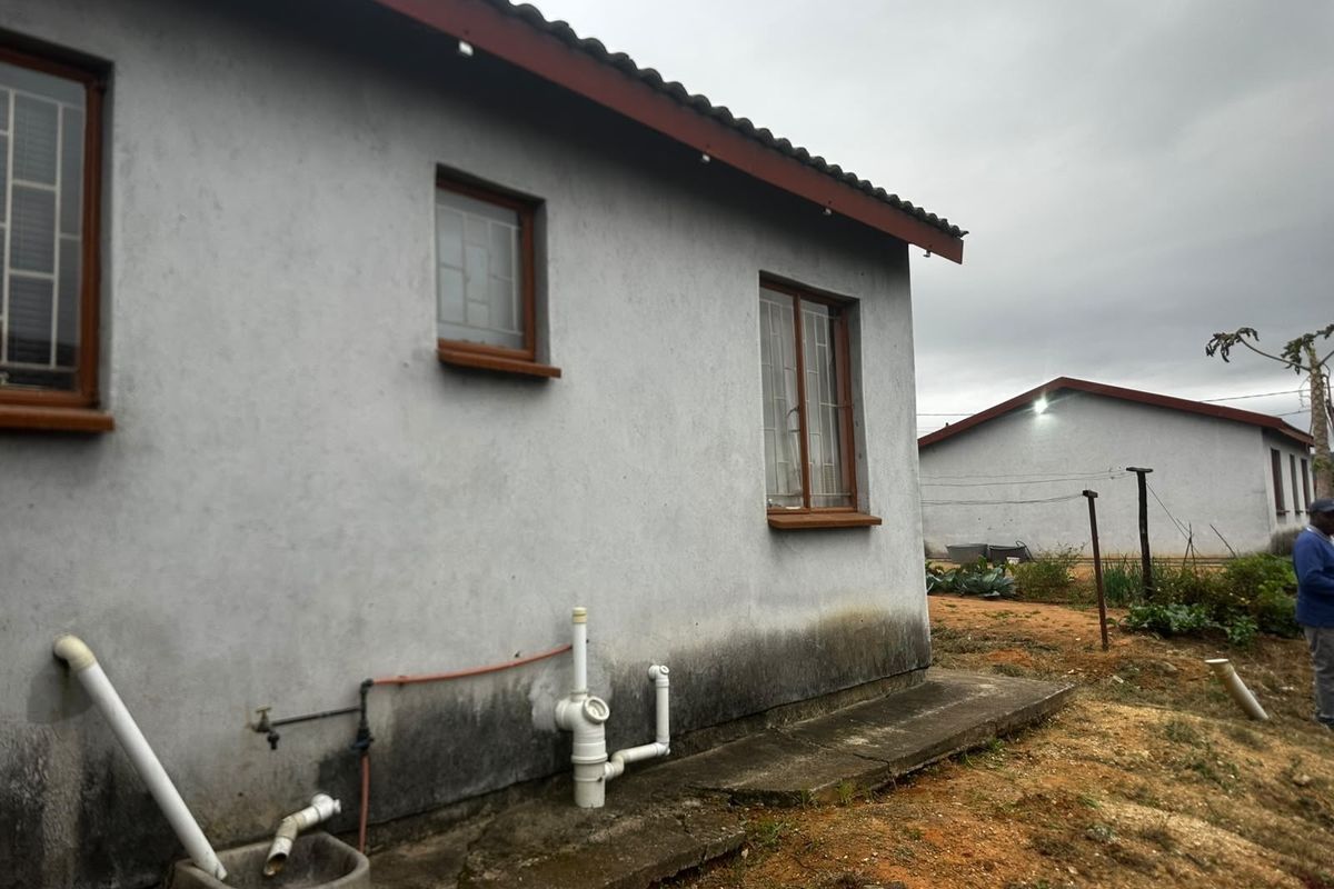 Rear exterior view of the property showing concrete apron, external plumbing fixtures, and visible signs of rising damp on the lower wall sections.