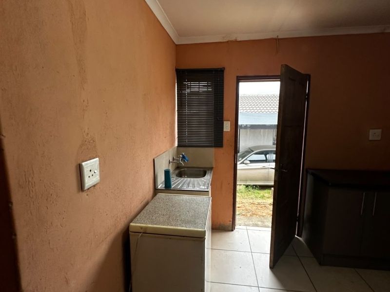 A compact kitchen area featuring tiled flooring, a stainless steel sink, and built-in cabinetry, with direct access to the exterior.
