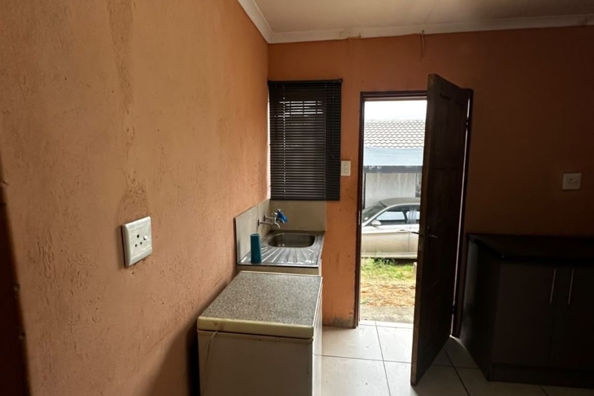 A compact kitchen area featuring tiled flooring, a stainless steel sink, and built-in cabinetry, with direct access to the exterior.