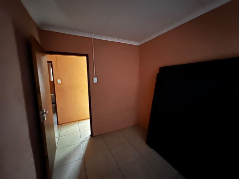 An empty bedroom featuring tiled flooring and peach-colored walls, with an internal door leading to an adjacent hallway.