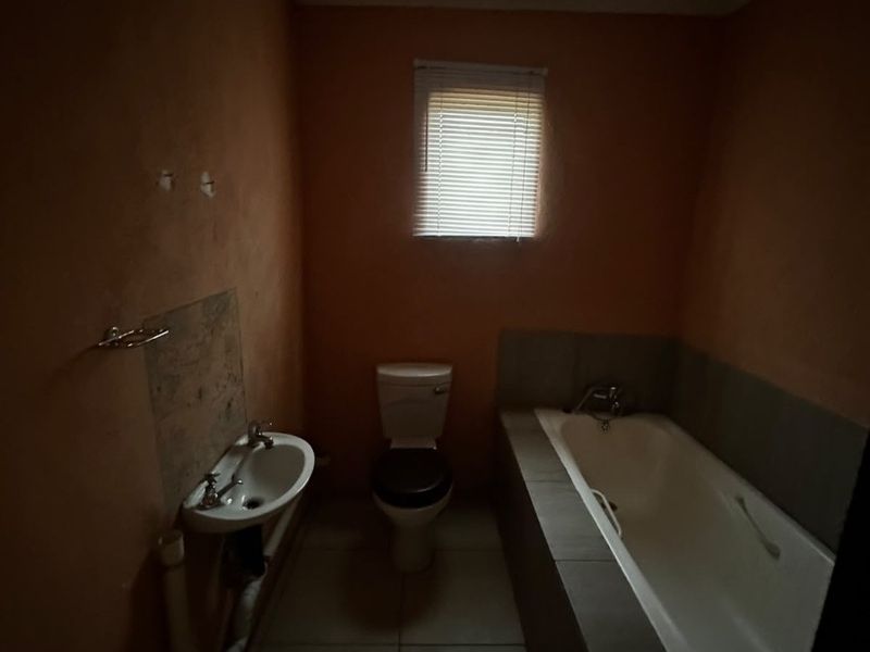 A basic bathroom featuring a bathtub, toilet, and washbasin with tiled flooring. The space is dimly lit and would benefit from cosmetic updates.