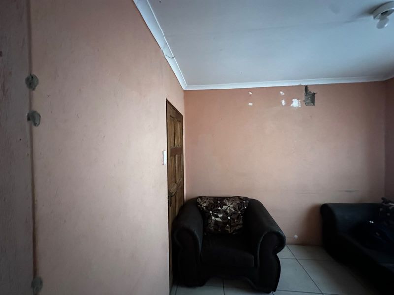 A living room area featuring tiled flooring and a timber door, currently requiring wall repairs and cosmetic updates to improve the overall finish.