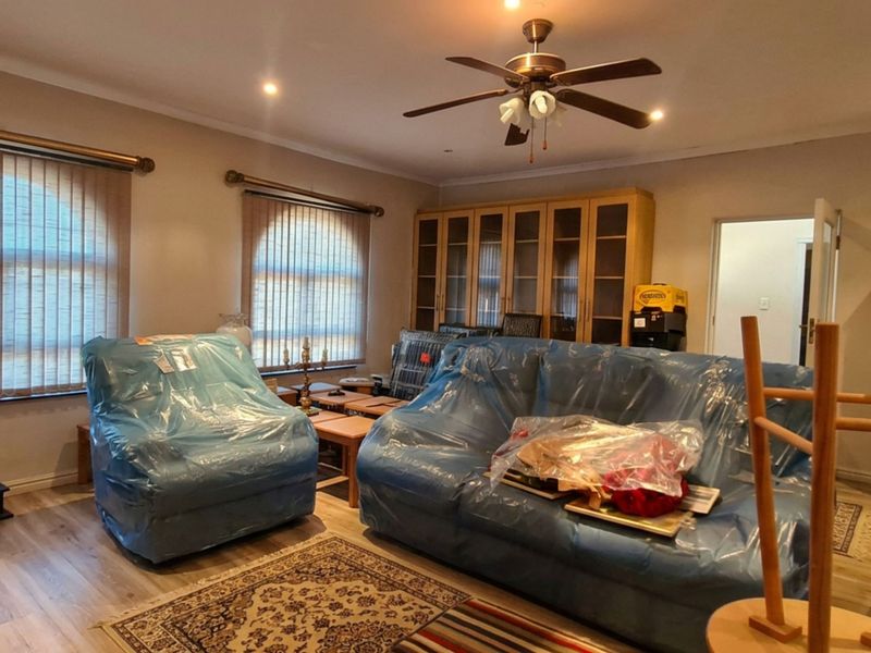A spacious living room featuring laminate flooring, recessed lighting, a ceiling fan, and built-in cabinetry, offering a functional layout with natural light from arch-top windows.
