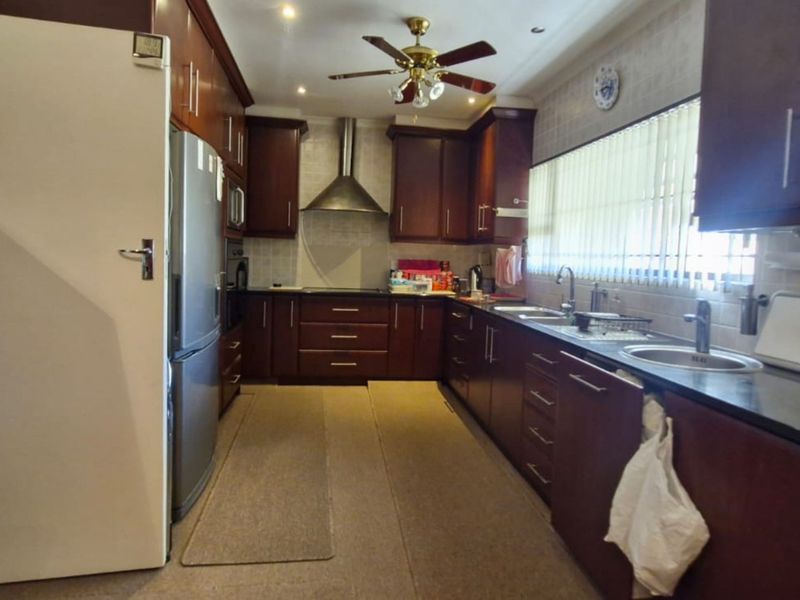 A functional kitchen featuring dark wood cabinetry, granite countertops, a stainless steel extractor fan, and a double sink with ample storage space.