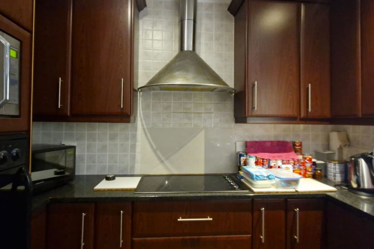 A functional kitchen featuring dark wood cabinetry, granite countertops, a stainless steel extractor fan, and a built-in microwave.
