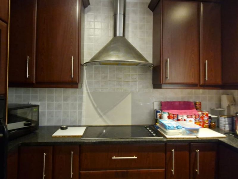 A functional kitchen featuring dark wood cabinetry, granite countertops, a stainless steel extractor fan, and a built-in microwave.