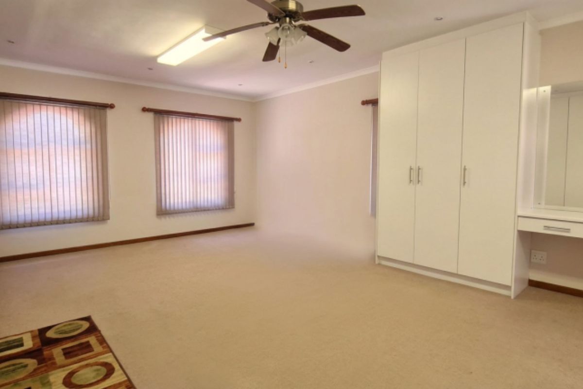 Spacious bedroom featuring neutral carpeting, extensive built-in cupboards, a dedicated vanity area, and ceiling fan, offering a clean and functional living space.