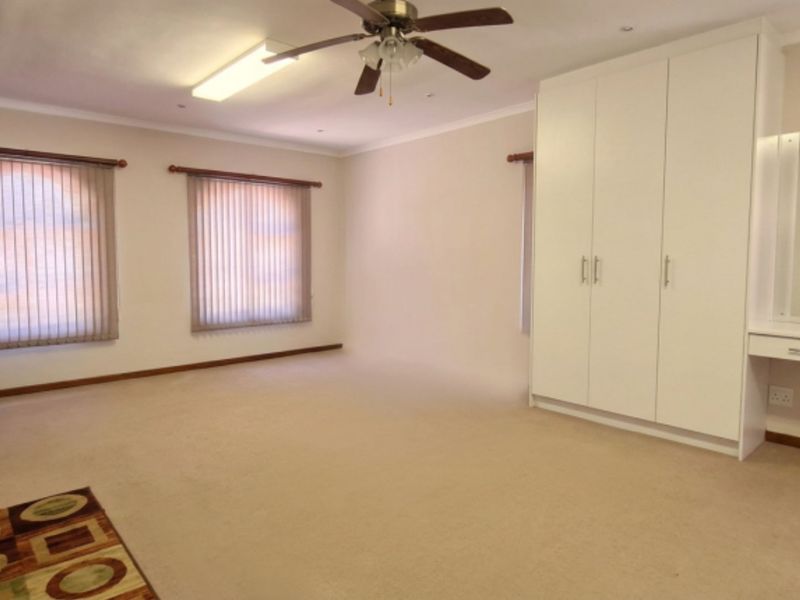 Spacious bedroom featuring neutral carpeting, extensive built-in cupboards, a dedicated vanity area, and ceiling fan, offering a clean and functional living space.