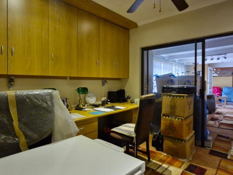 A home office featuring built-in wooden cabinetry and a desk, with a sliding glass door providing access to the adjacent living area.