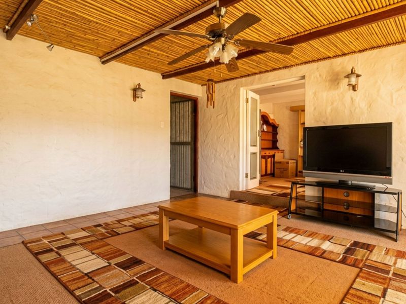 Living room featuring a rustic bamboo ceiling, ceiling fan, wall sconces, and tiled flooring, with access to an adjacent room.