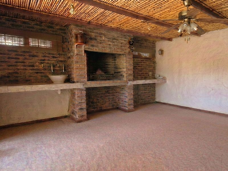 Covered patio area featuring a built-in brick braai, integrated sink, bamboo ceiling, and ceiling fan, offering a rustic entertainment space.